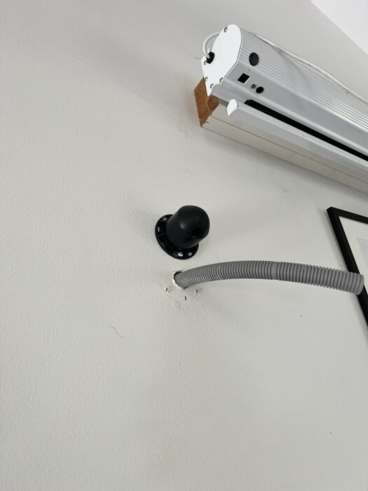 Hål i väggen med grå slang och monterad enhet, del av dold kabeldragning för högtalare.