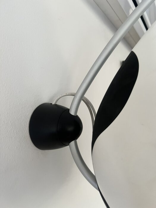 Svart och vit lampskärm monterad på väggen med ett dolt kabelrör i bakgrunden.