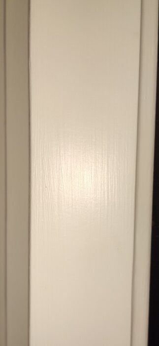 En närbild av ett nymålat fönster, där penseldrag och blank färgyta syns tydligt med blixten från en mobilkamera.