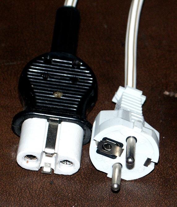 Svart och vit apparatkontakt med jordbleck, svår att hitta nuförtiden, visas på brun yta.