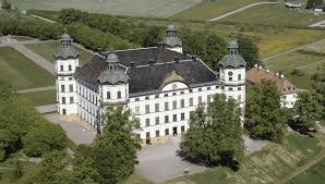 Skokloster slott, ett stort vitt barockslott med torn, omgiven av grönska och landskap, sett från ovan.