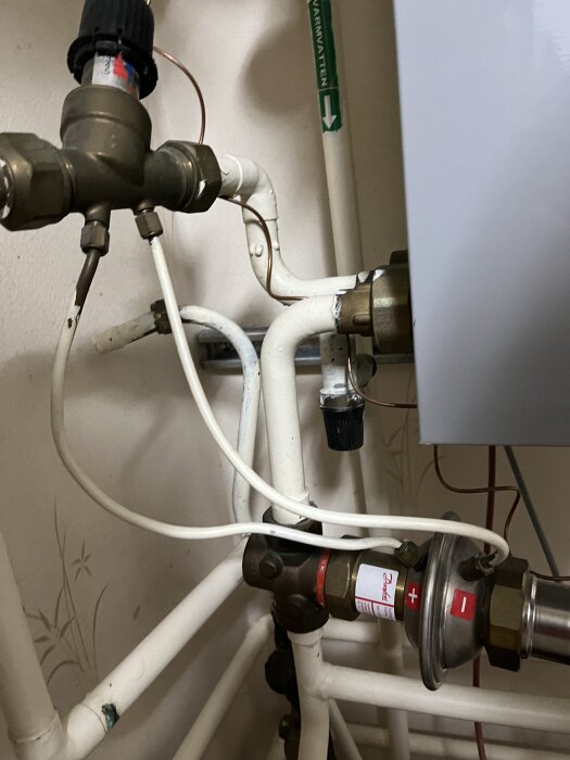 Vattenrör och ventiler i ett byggnadstekniskt system med märkt ledning för varmvatten, kopplingar och tryckregulator.