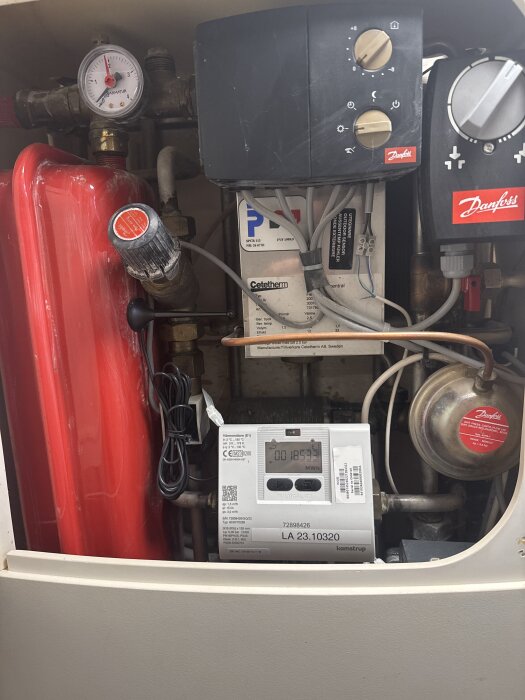 Värmepanna med tryckmätare och termostat, visar flera ventiler och röranslutningar, röda och svarta komponenter, inklusive varumärket Danfoss.