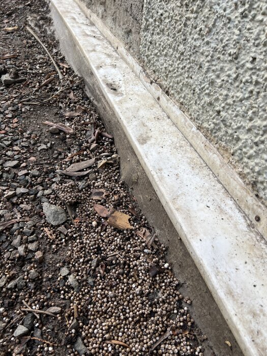 Bild av husvägg med markduk, mur och jordblandning i förgrunden med stenar och organiskt material.