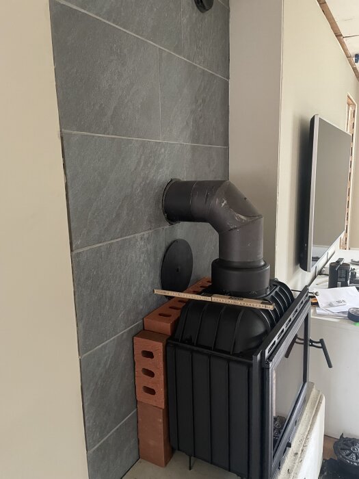 Insatskamin med rökkanal monterad, omgiven av tegelstenar och måttstock, på väg att byggas in i en murspis för bättre värmefördelning.