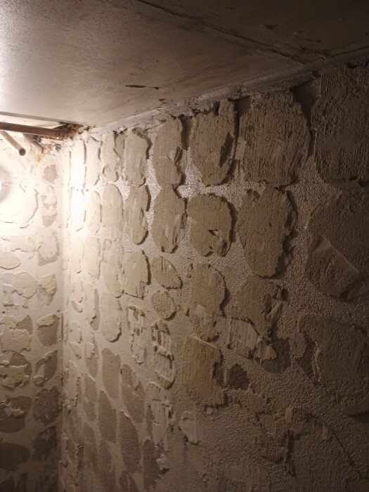 Vägg i källare med bortbilat kakel och kvarvarande gammal fix, ojämna ytor synliga.