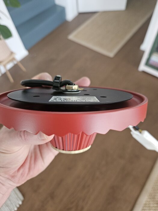 Röd lampsockel hålls i handen, designad för att monteras direkt mot taket utan att hänga ner från eluttaget.