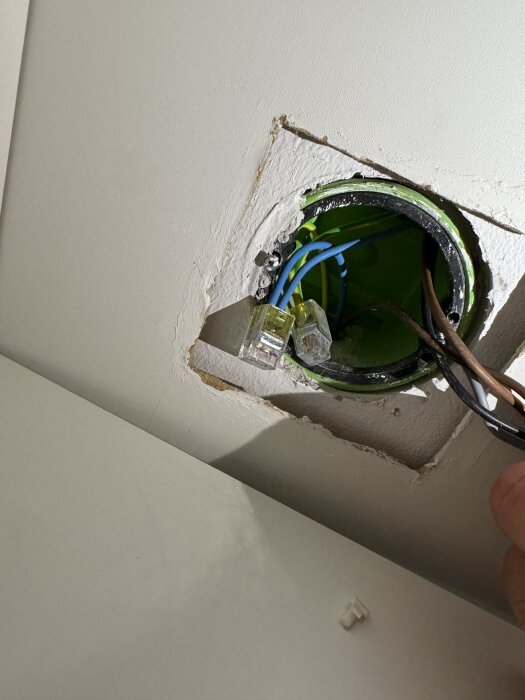 Elektrisk kopplingsdosa med blå och bruna ledningar, där blå förmodas vara neutral men handen har inte anslutit den än.