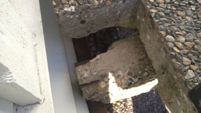 Närbild av en betongtrappa med synlig spricka och armering vid kanten nära en träregel och fasadvägg.