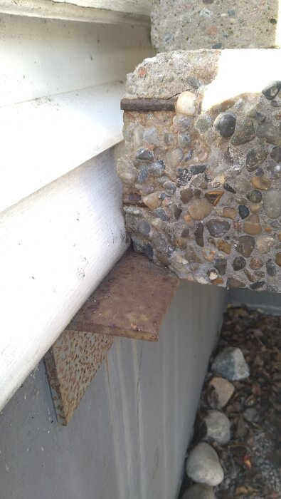 Närbild av betongtrappa vid husvägg med synliga armeringsjärn och sprickor; rostig metallplatta undertill.