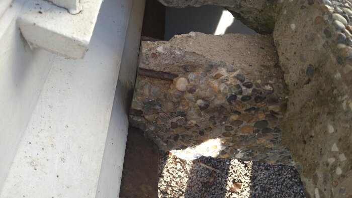 Skadad betongtrappa med synliga armeringsjärn vid sidan av ett vitt hus, tecken på att vatten har trängt in och orsakat sprickor.