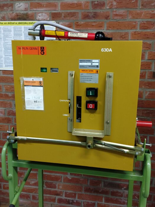 Merlin Gerin Fluarc FG 1 Effektbrytare 12kV 630A från 1988, monterad på en grön ställning framför en tegelvägg.