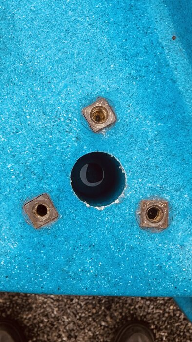 Blått båtunderlag med tre runda bronsfästen runt ett centralt borrat hål.