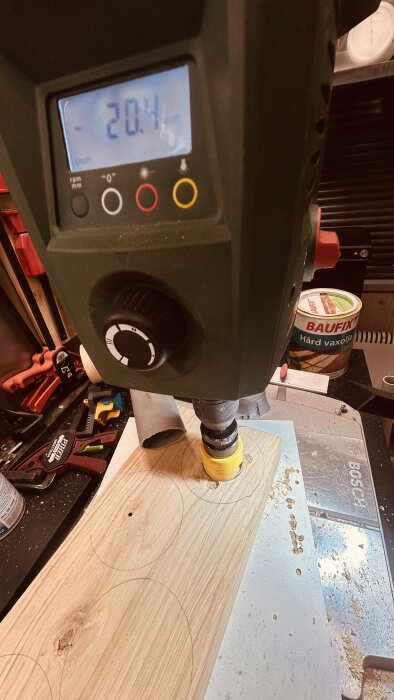 Bosch PBD-40 bänkborrmaskin borrar cirklar i en tjock ekplanka, med en digital skärm som visar borrdjupet, och Baufix olja i bakgrunden.