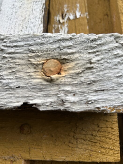 Äldre trätavla med en rostig spik inslagen, del av en byggstruktur från 1944.