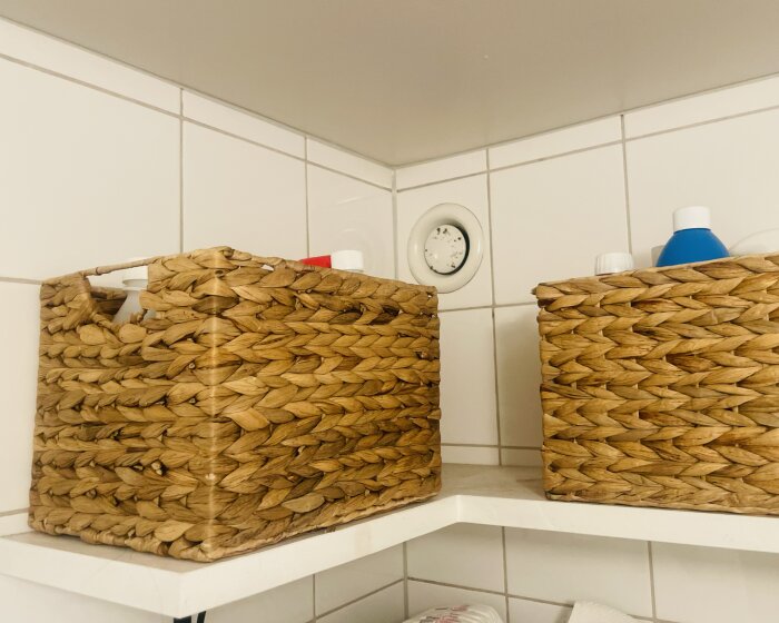 Korgar på hylla i badrum med vitkaklade väggar och en ventil synlig bakom.
