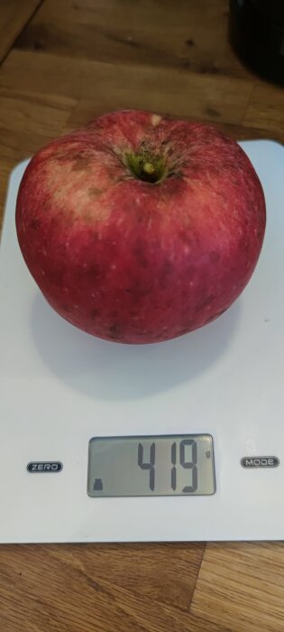 Rött äpple på en vit köksvåg som visar vikten 419 gram.