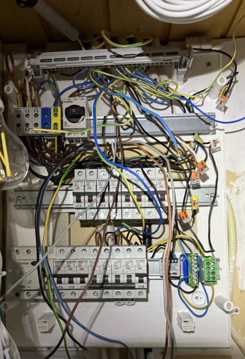 Elcentral med många färgglada kablar och säkringar, inklusive brytare och terminaler, monterad på vägg i trästruktur.