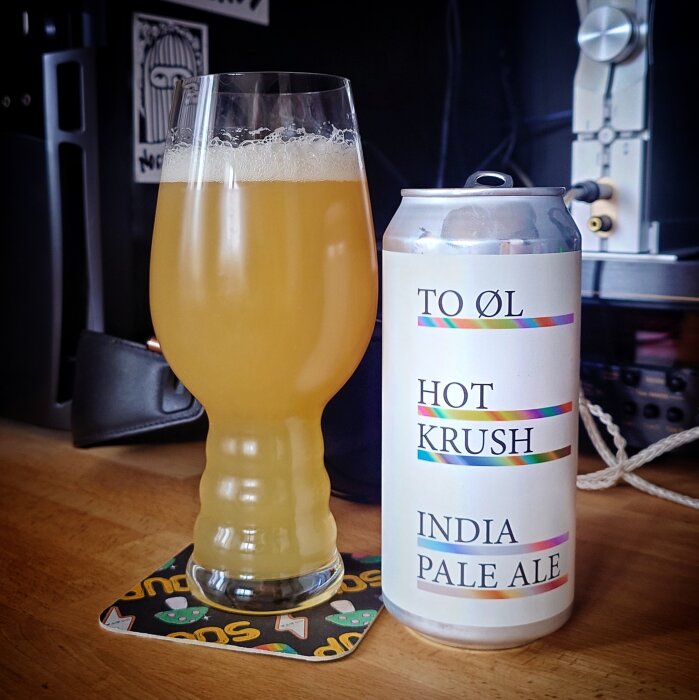 En glas fylld med ljus IPA och en burk märkt "To Øl Hot Krush India Pale Ale" på ett bord.