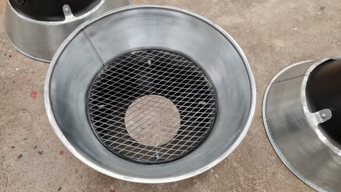 Tre metalltrattar med svetsutsug och galler ligger på golvet, klara för testning av förbättrad rökavledning inom svetsprocesser.