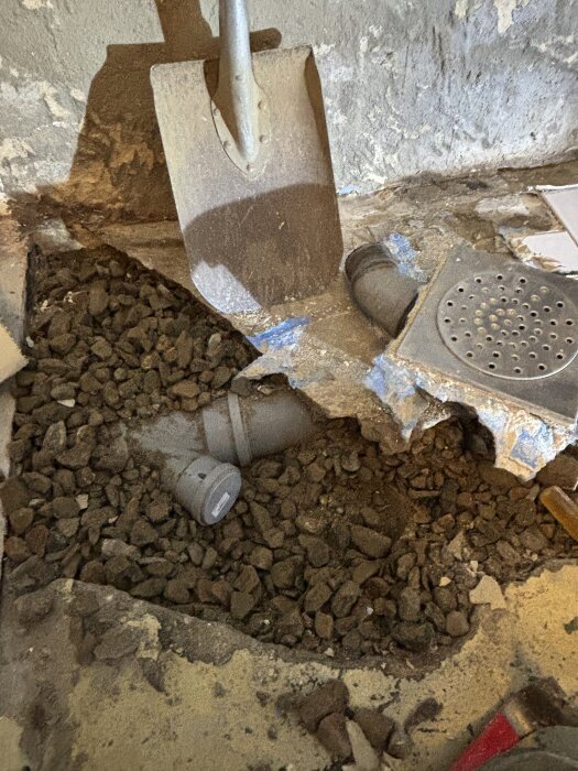 Spade bredvid demolerad duschbrunn fylld med grus och gamla rör.