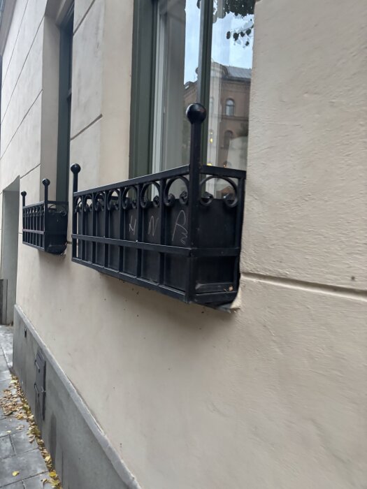 Svarta järnblomlådor monterade på utsidan av en byggnadsfönster vägg i stadsmiljö.