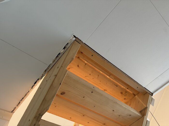 Trästruktur av blivande räckesdelar under konstruktion i ett husprojekt, med träbalkar mot vitt tak.