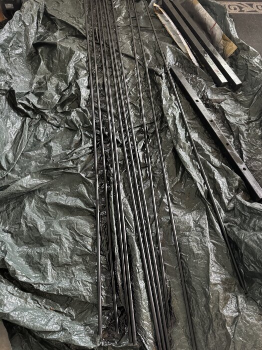 Svarta metallstänger och balkar ligger på en grön presenning, förberett för att bli delar av ett räcke.