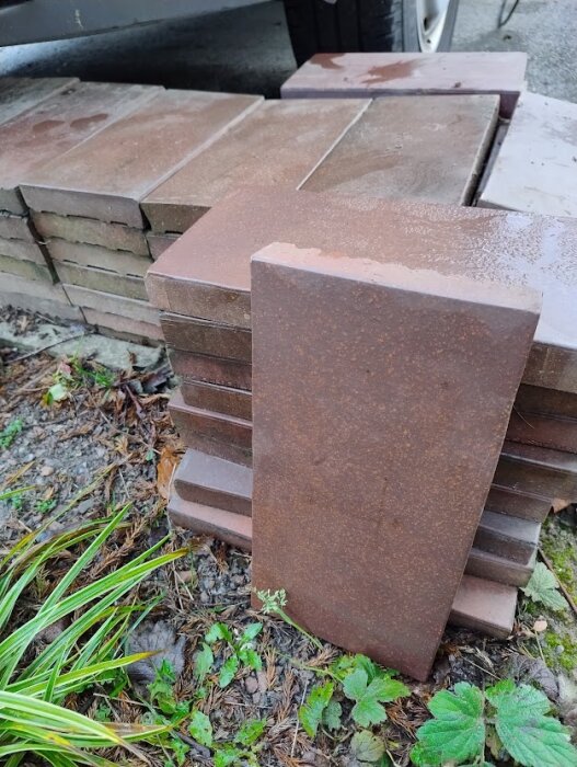 Bruna Höganäs klinkerplattor staplade utomhus på marken, delvis fuktiga efter regn.