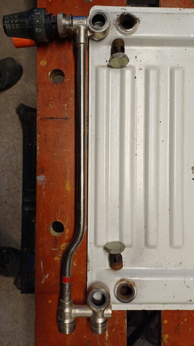 Gammal AGA Termopanel-radiator med demonterat kopplingsrör och ventil på ett träbord.