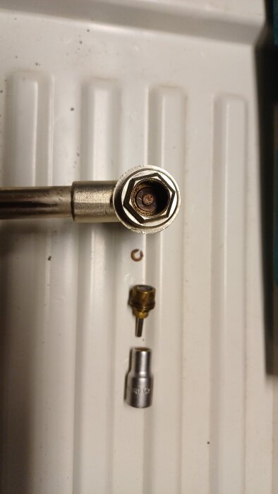 Gamla ventilkomponenter utplacerade på en vit yta; delar av en demonterad termostatisk ventil från ett värmesystem syns tydligt.