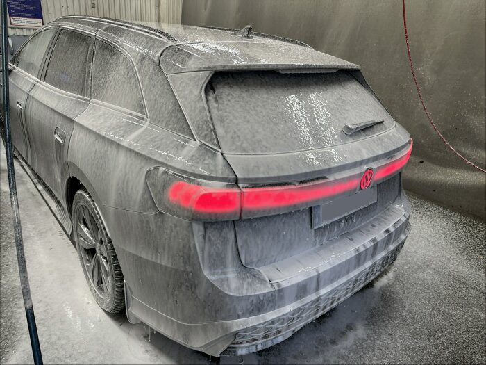 En bil i en tvätthall täckt med skum, sett bakifrån, med bakljusen synliga.