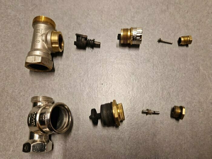 Demonterade delar av Danfoss och MMA ventiler, inklusive ventilinsatser, packboxar och låsring på stiftet, placerade på en yta.