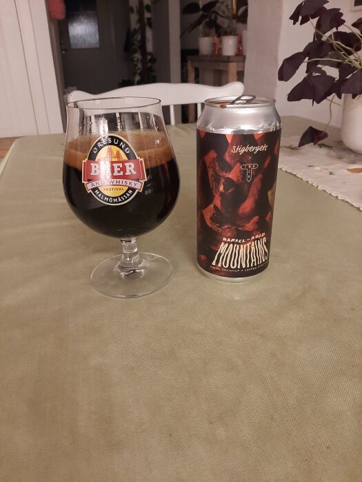Glas med Stout öl från Stigbergets och en burk bredvid, serverat på ett bord med en växt i bakgrunden.