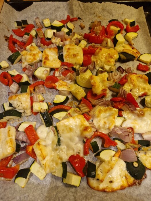 Ugnsrostade grönsaker med zucchini, paprika, rödlök och smält halloumi på bakplåtspapper.
