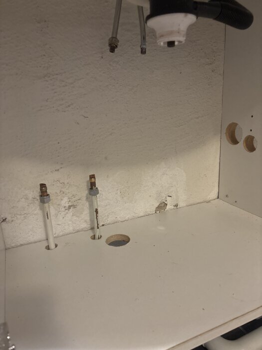 Rörinstallation under bänkskiva med synliga rördragningar, inklusive två vertikala rör som kommer upp genom hål i ytan.