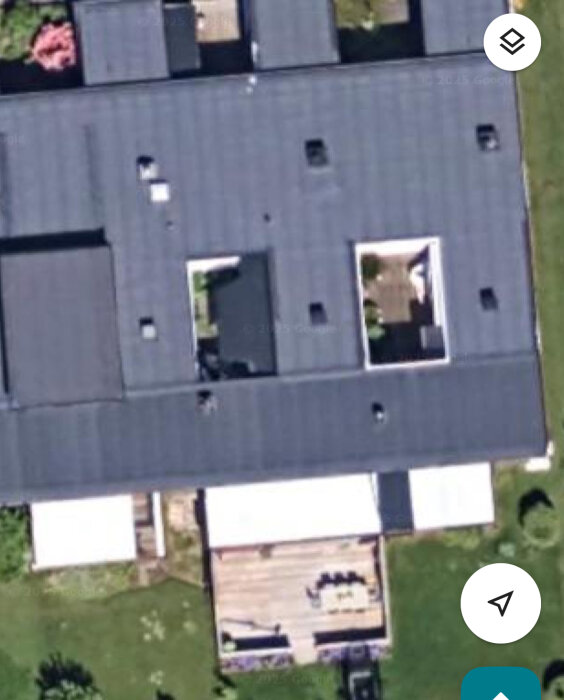 Flygfoto över en fastighet med papptak och en öppen atriumgård i mitten, omgiven av trädäck och grönska.