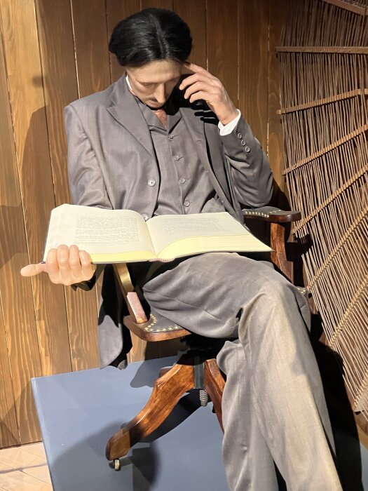 Man i en grå kostym sitter i en stol, lutar huvudet på handen och håller en öppen bok.