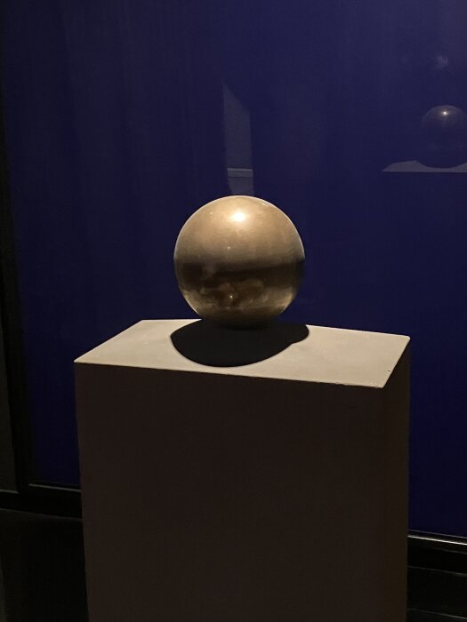 En glänsande metallisk sfär på en piedestal mot en mörk bakgrund.