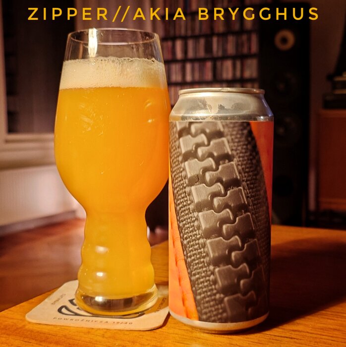 Ett glas med orangefärgad öl bredvid en burk med blixtlåsdesign på etiketten, texten "ZIPPER//AKIA BRYGGHUS" ovanför.