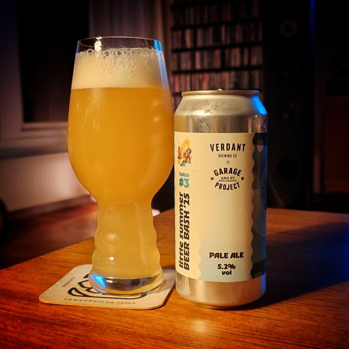 Ett glas med skummande öl och en burk Verdant Pale Ale står på ett bord inomhus.