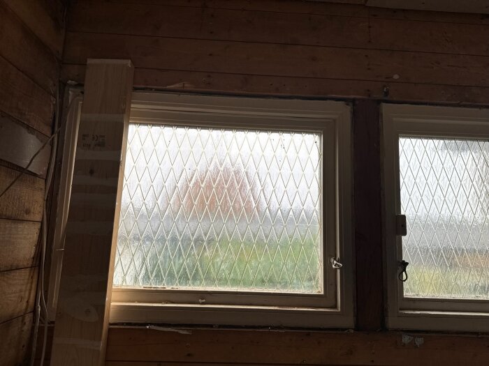 Två blyinfattade fönsterrutor i ett träbeklätt rum, där renovering pågår.