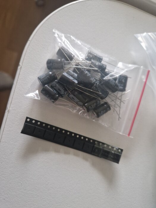 På bilden syns en plastpåse med kondensatorer och en remsa med elektroniska komponenter på ett bord.