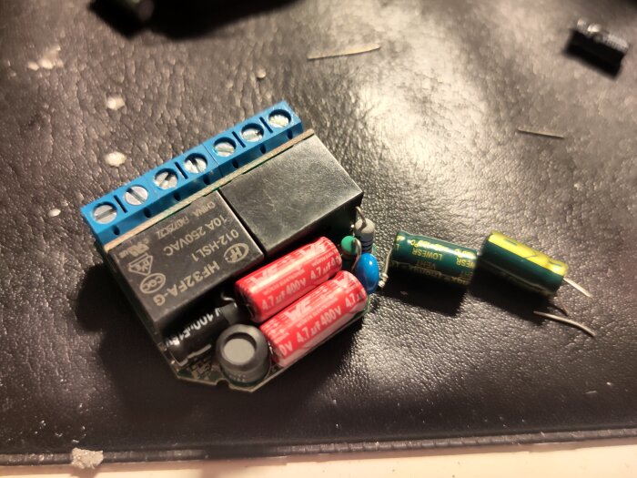 Elektronisk enhet med utbytta kondensatorer på en arbetsyta, inklusive Shelly-komponenter och lösa kondensatorer.
