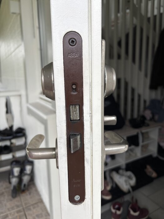 Ytterdörrs låshus med texten "Assa" och "Reko SYM", typiskt för hus från 90-talet, visas med handtag och dörrmiljö i bakgrunden.