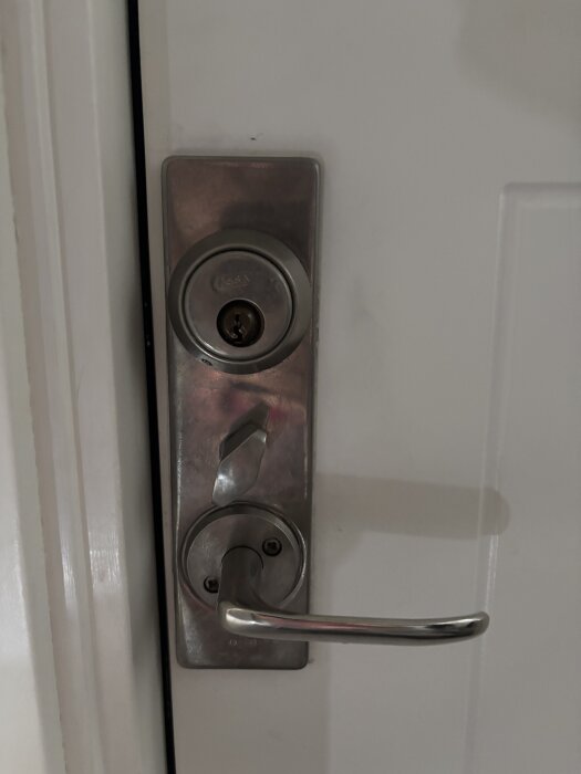 Ytterdörr med äldre cylinderlås och dörrhandtag i metall.