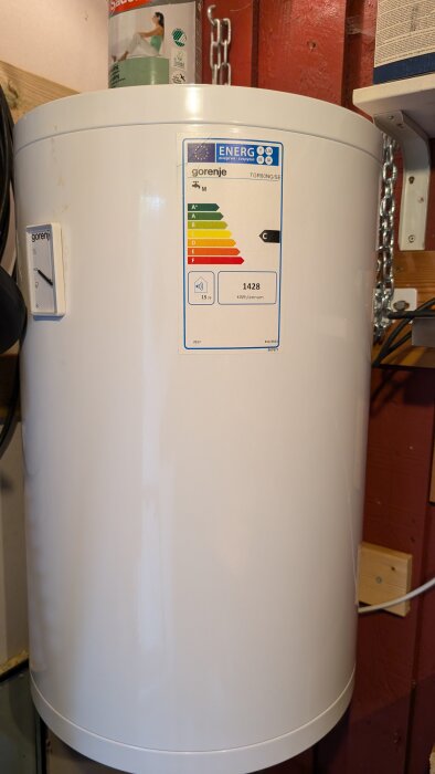 Vit varmvattenberedare av märket Gorenje med energimärkning C och effektförbrukning 1428 kWh/annum, placerad i ett förråd.