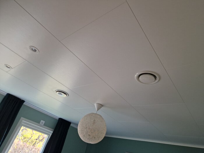 Tak med ventilationsdon för till- och frånluft samt en taklampa, i ett rum med gröna väggar och fönster med mörka gardiner.