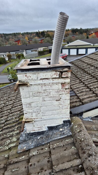 Vit tegelstensskorsten med böjd metalltub ovanpå taket, omgiven av höstlandskap.