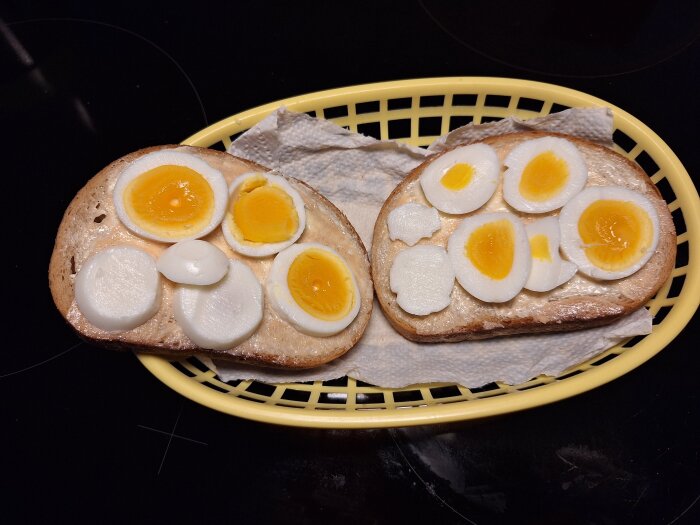 Äggsmörgåsar med skivad kokt ägg på rostat bröd i en gul korg, serverade på hushållspapper.